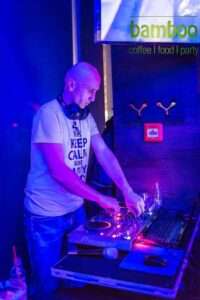 tomislav 4 DJ Tomislav (Tom Black) nasmiješen ispred DJ pulta, okružen plesnim svjetlima i razigranom atmosferom na vjenčanju.